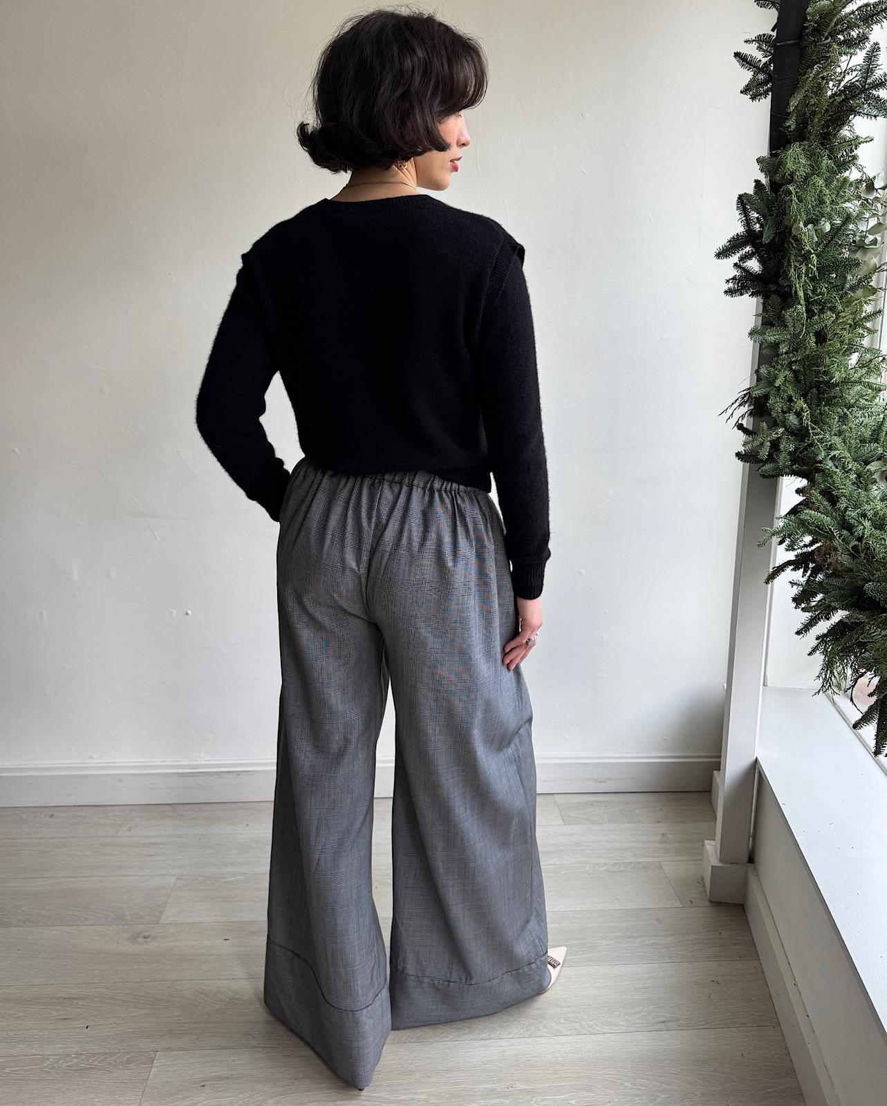 Back view of stunning pair of grey wide-leg check wool trousers by Michael Lo Sordo. They feature an elasticated waistband at the back, a pleated front, and wide cuffs.