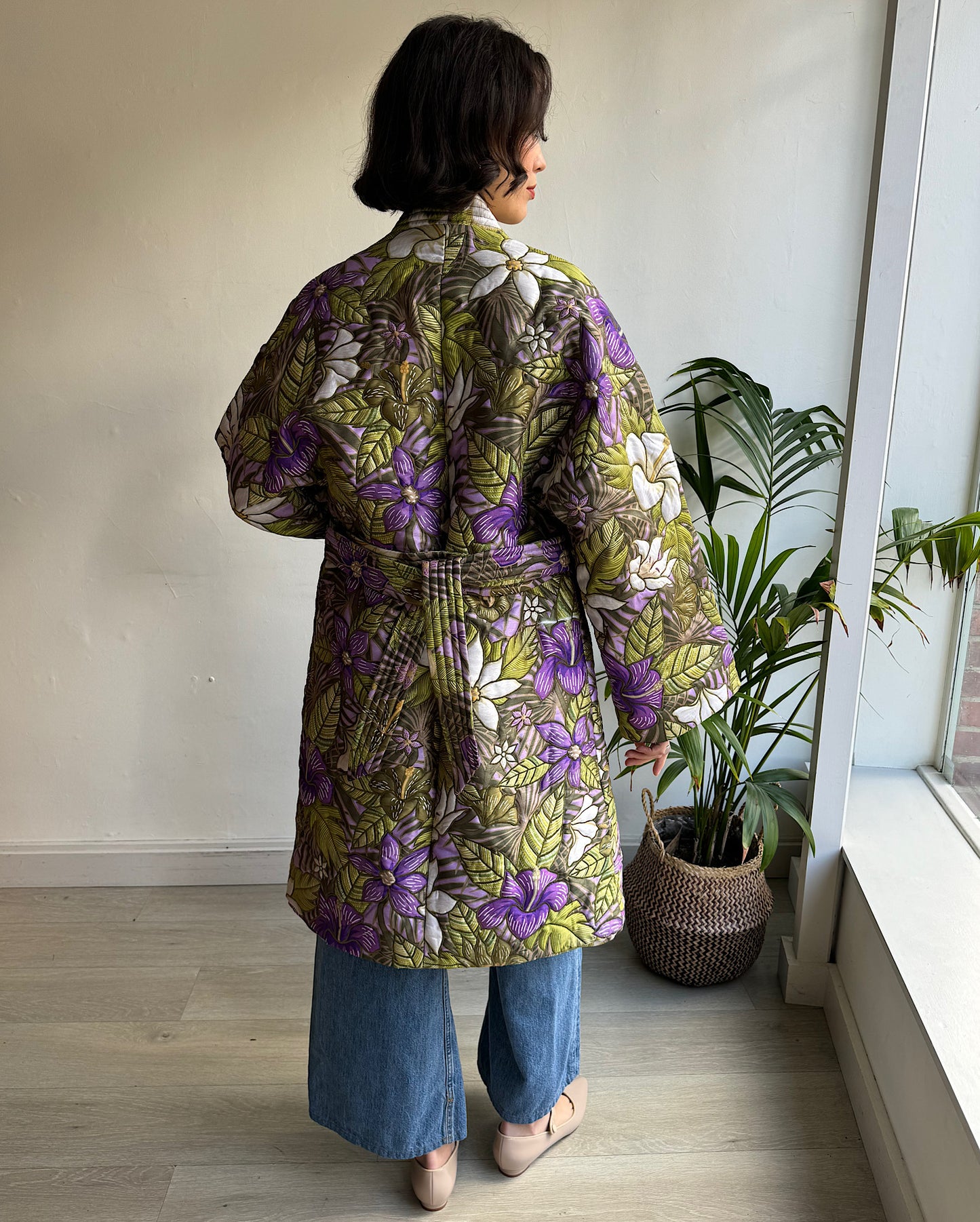 Back view of Tropical Hibiscus Quilted Coat by Hayley Menzies. This luxurious outerwear piece features a striking floral hibiscus print, bringing a burst of tropical charm to your wardrobe. The beautifully quilted design ensures both warmth and comfort, making it a perfect choice for cooler months without sacrificing style.