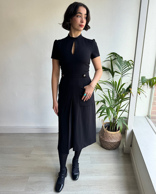 Front view of timeless black dress features chic short sleeves, a sophisticated high neck adorned with a delicate keyhole detail, and a discreet hidden back zipper, ensuring a seamless and flattering fit. Made by Ba&sh.