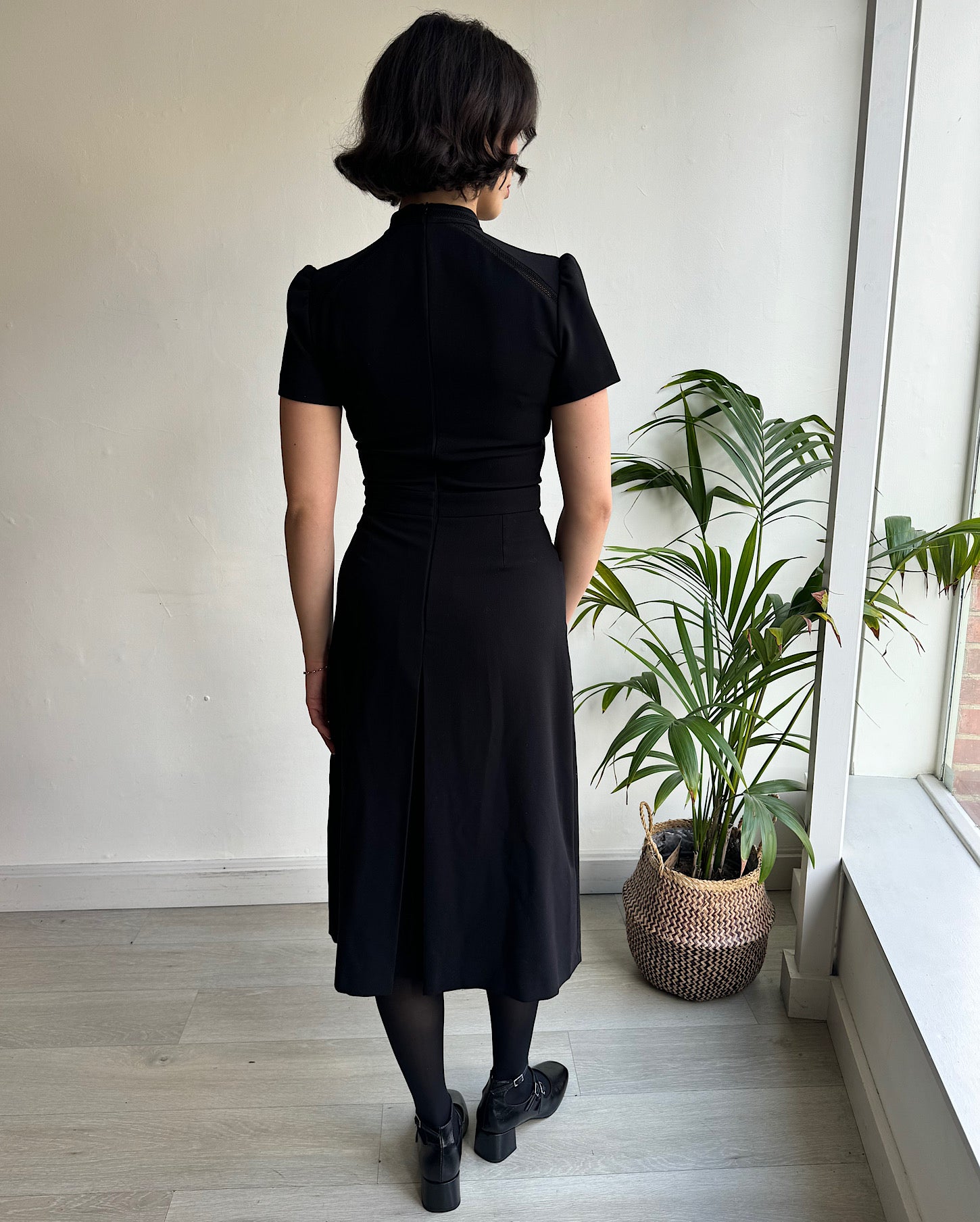 Back view of timeless black dress features chic short sleeves, a sophisticated high neck adorned with a delicate keyhole detail, and a discreet hidden back zipper, ensuring a seamless and flattering fit. Made by Ba&sh.