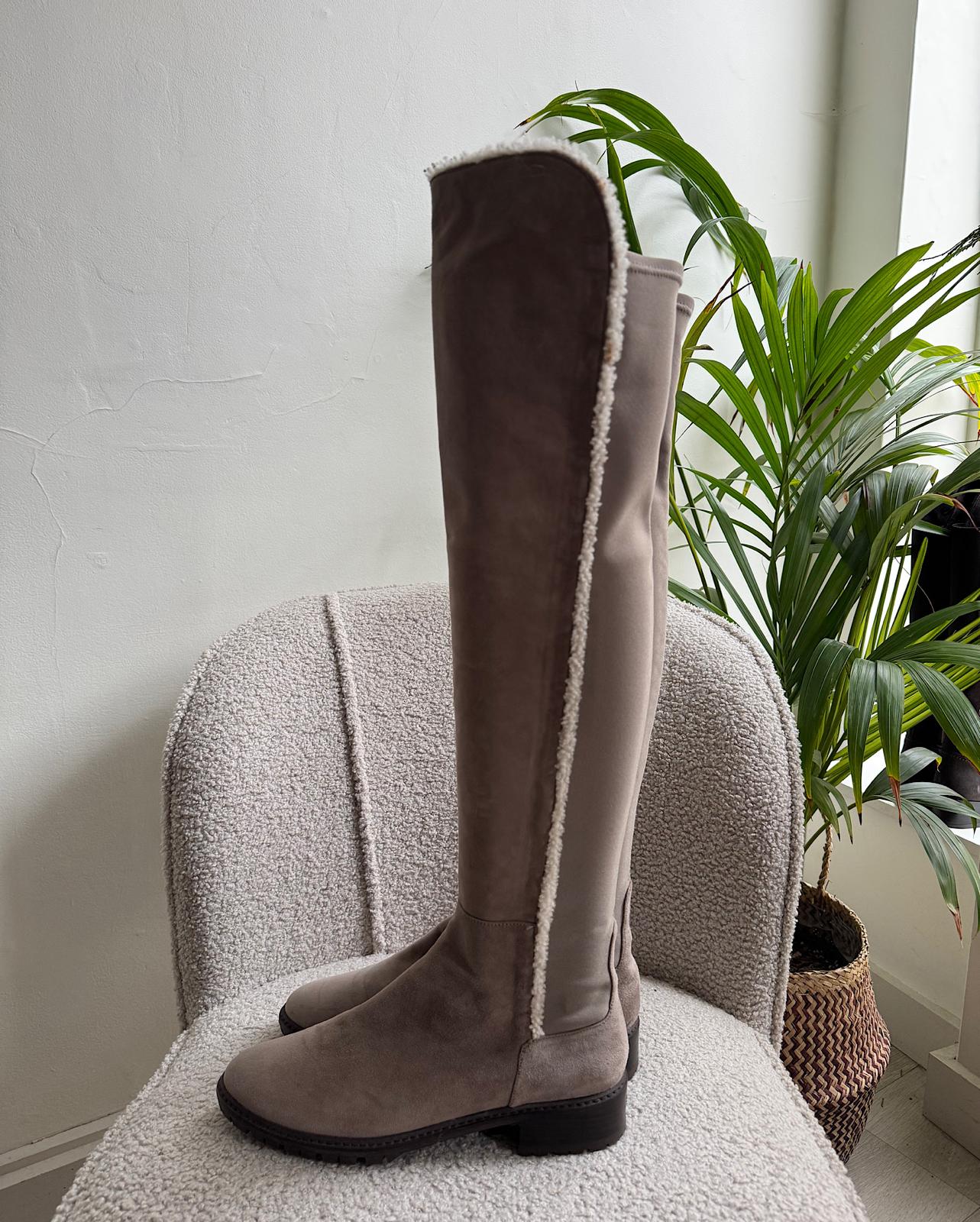 Side view of fashionable pair of suede parka over-the-knee boots from Stuart Weitzman, featuring a shearling trim