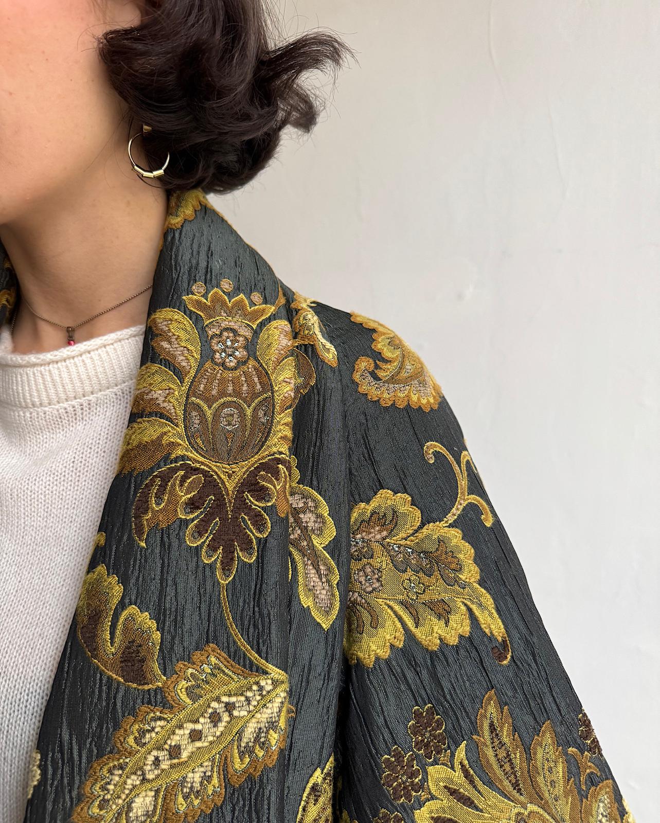 Close up of elegant drape-front jacket by Antonio Marras features a gold pattern on dark green fabric