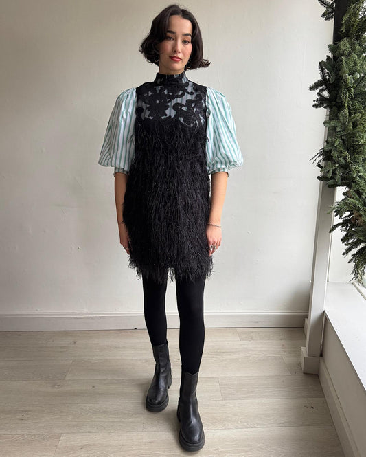 Front view of baroque layered dress by Ganni features exaggerated puffed sleeves and sparkly faux feather trims, designed to look like a dress layered over a striped shirt.