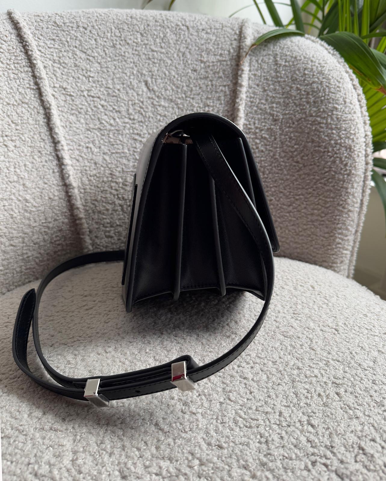 Side view of expertly crafted Le Papa crossbody bag by Alaia features a sleek black leather construction complemented by silver-tone hardware.